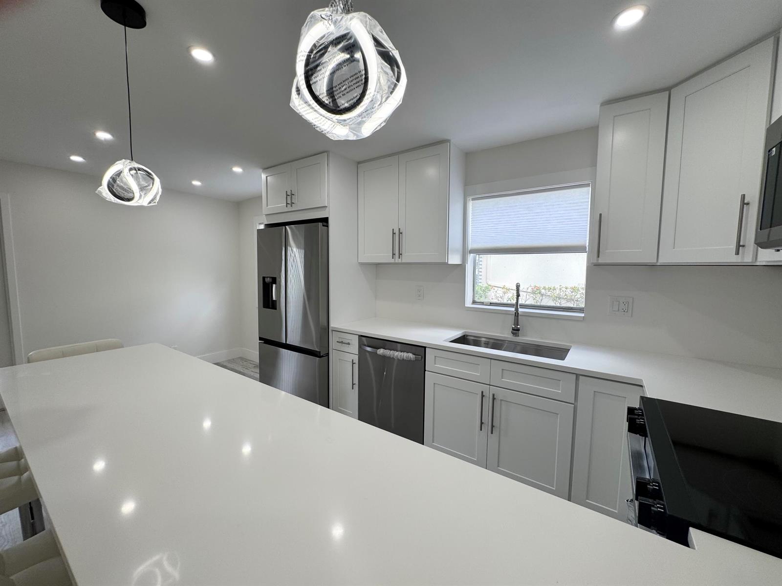 A modern kitchen features white cabinetry, stainless steel appliances, and a large quartz island — 108 Brittany # C, Delray Beach FL 33446, DELRAY BEACH, FL
