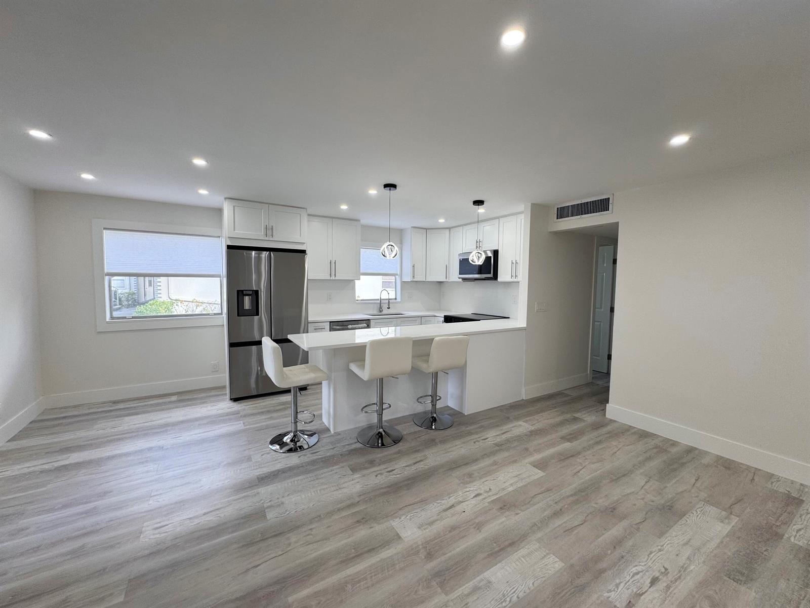 A modern kitchen features white cabinetry, stainless steel appliances, and a breakfast bar with stools — 108 Brittany # C, Delray Beach FL 33446, DELRAY BEACH, FL
