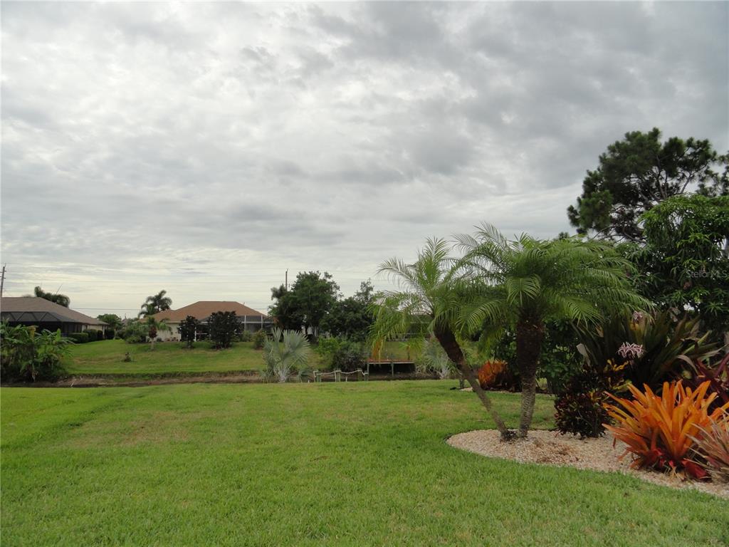 A grassy backyard features a small canal, palm trees, and neighboring houses under a cloudy sky — 428 BOUNDARY BOULEVARD, ROTONDA WEST, FL