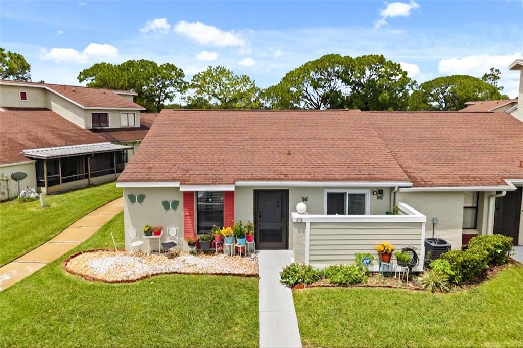An exterior view of a single-story attached home with a brown roof and front patio — 49 PINE ISLAND CIRCLE, KISSIMMEE, FL