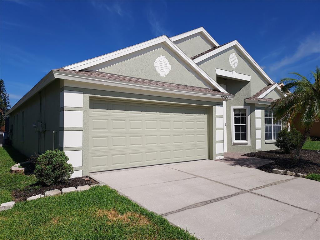 A single-story house with a two-car garage, light green stucco walls, and white trim — 12603 MIDPOINTE DRIVE, RIVERVIEW, FL