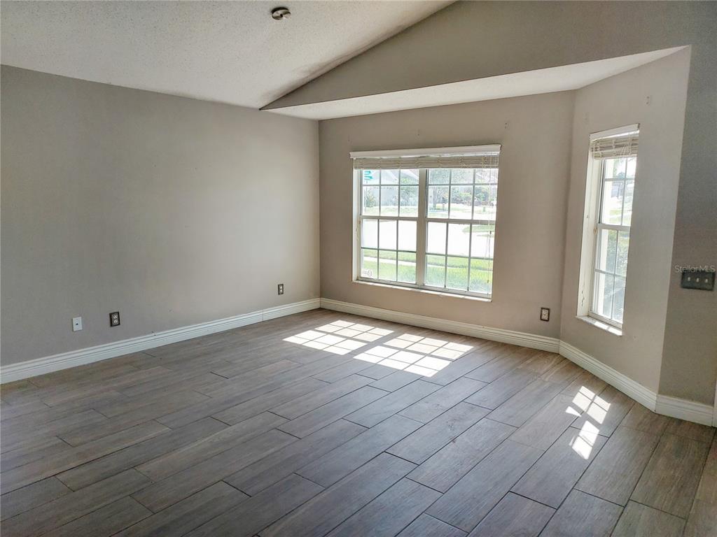 An empty room features light-colored walls, wood-look tile flooring, and a vaulted ceiling — 12603 MIDPOINTE DRIVE, RIVERVIEW, FL