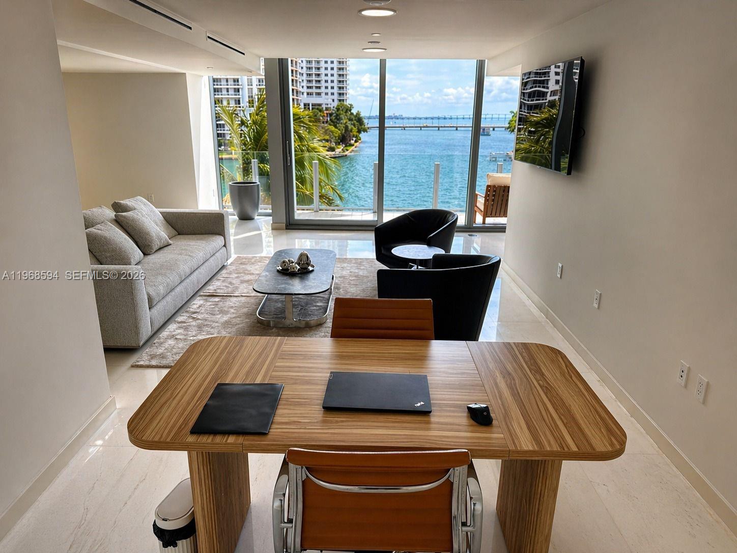A modern living and dining area features a waterfront view through floor-to-ceiling windows — 300 Biscayne Blvd Way # 303, Miami FL 33131, MIAMI, FL