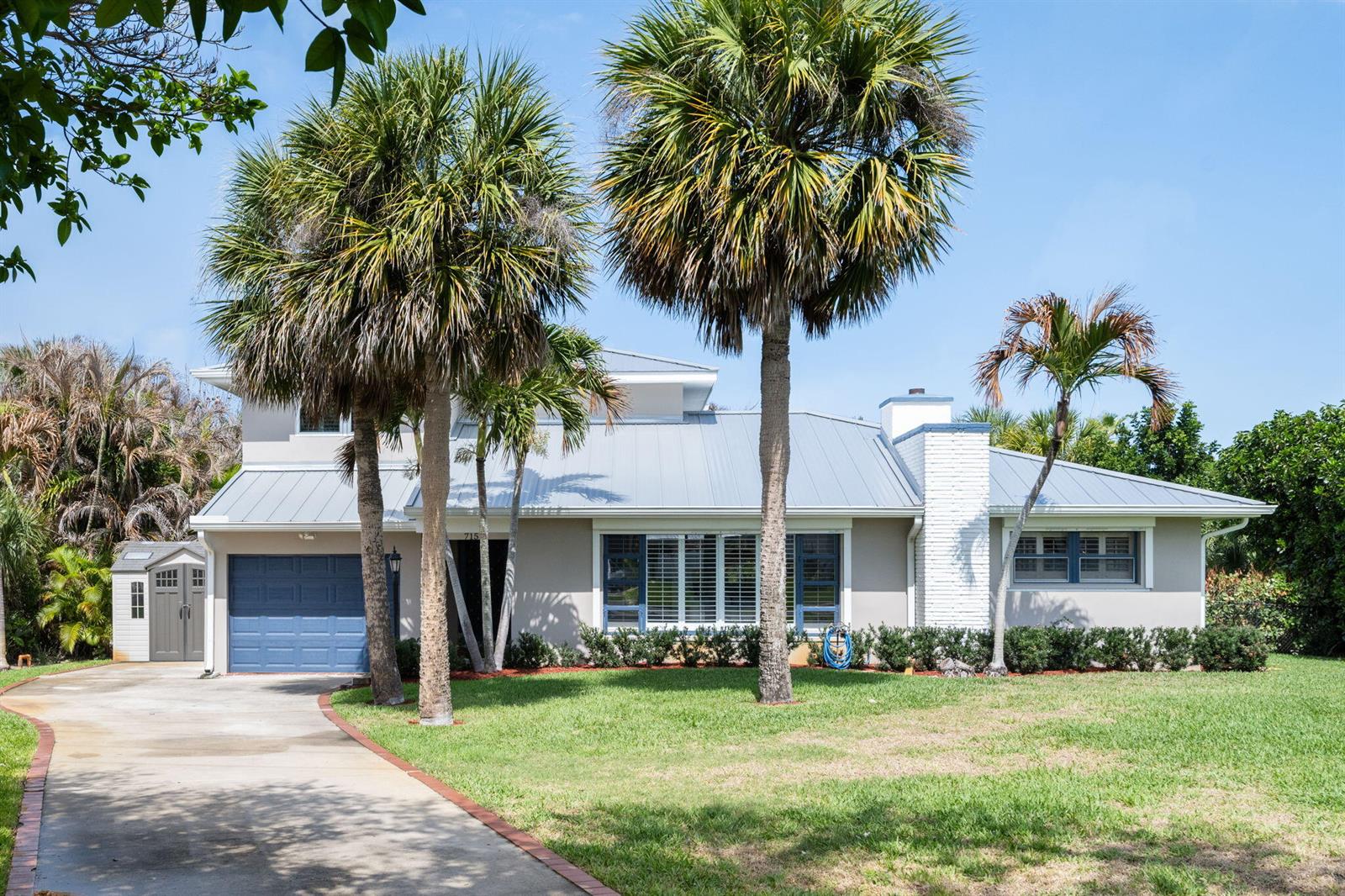 A single-story house with a metal roof, blue garage door, and two large palm trees — 715 Conn Way, Vero Beach FL 32963, VERO BEACH, FL