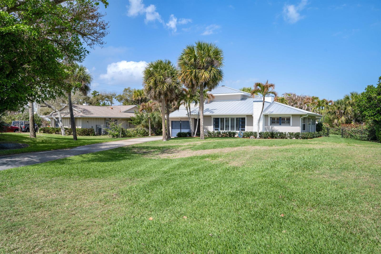 A single-story house with a metal roof and palm trees sits behind a large lawn — 715 Conn Way, Vero Beach FL 32963, VERO BEACH, FL