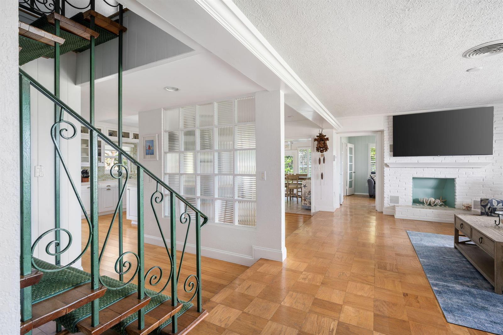 A living room features parquet wood flooring, a brick fireplace, and a green metal staircase — 715 Conn Way, Vero Beach FL 32963, VERO BEACH, FL