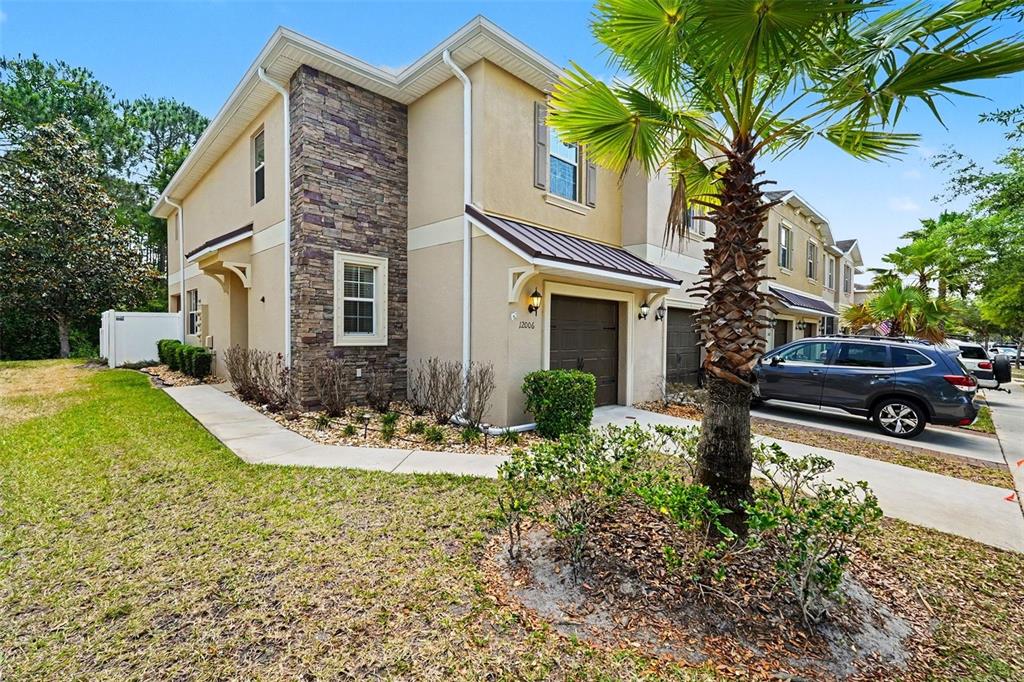A two-story townhouse with a stone facade, tan stucco walls, and a single-car garage — 12006 GREENGATE DRIVE, HUDSON, FL
