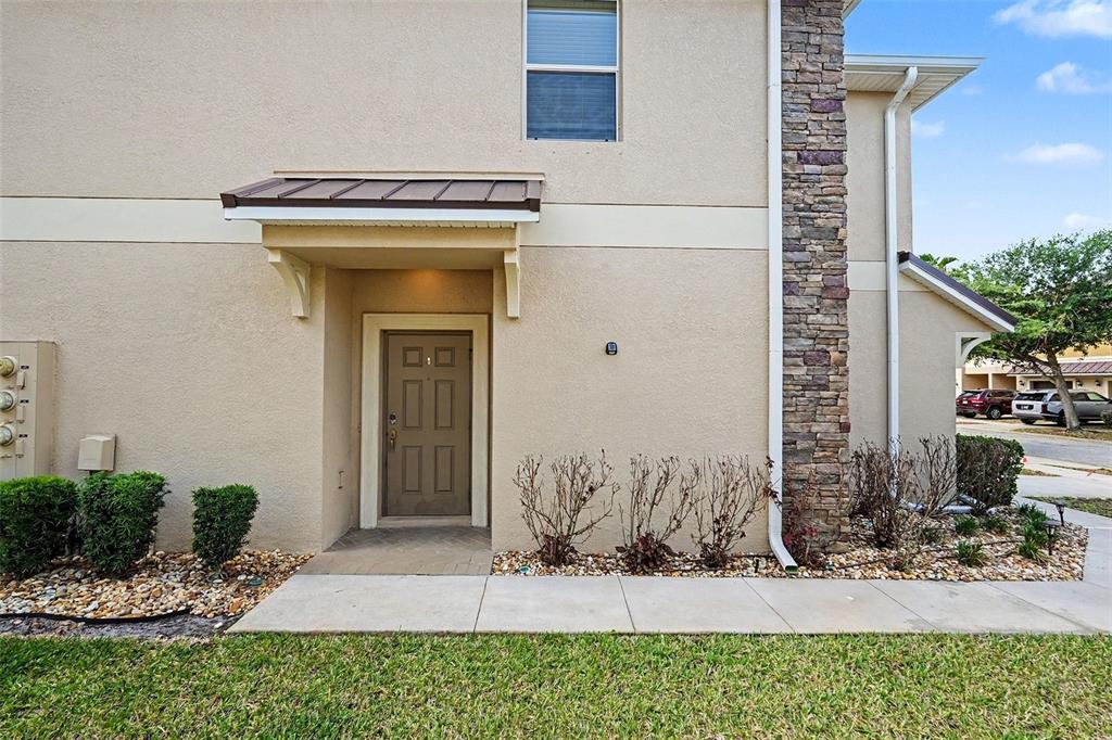 The exterior of a tan stucco townhouse features a brown front door and stone accents — 12006 GREENGATE DRIVE, HUDSON, FL