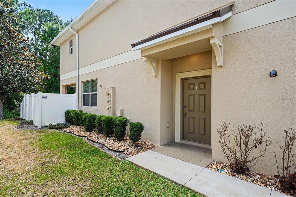 The exterior of a beige two-story townhouse features a brown front door and landscaping — 12006 GREENGATE DRIVE, HUDSON, FL