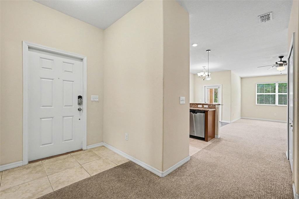 An entryway with tile flooring leads into a carpeted living area and an open kitchen — 12006 GREENGATE DRIVE, HUDSON, FL