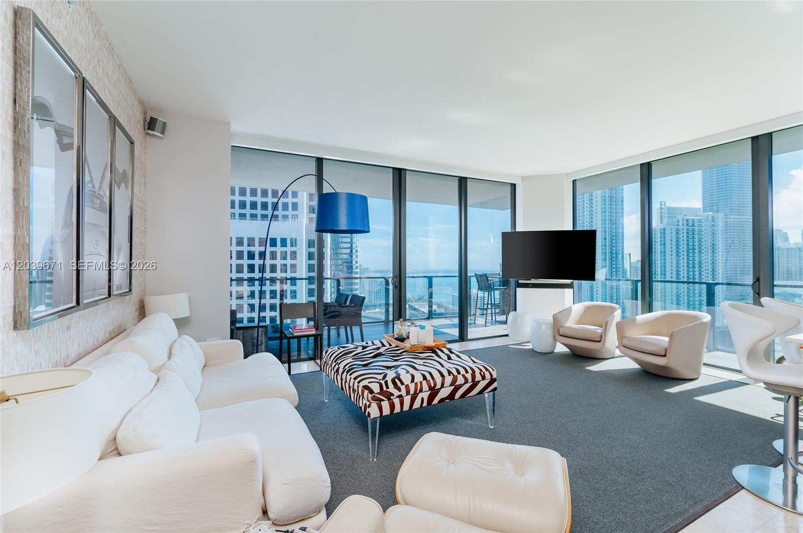 A modern living room features a zebra-print ottoman, white seating, and floor-to-ceiling city views — 68 SE 6th St # 2601, Miami FL 33131, MIAMI, FL