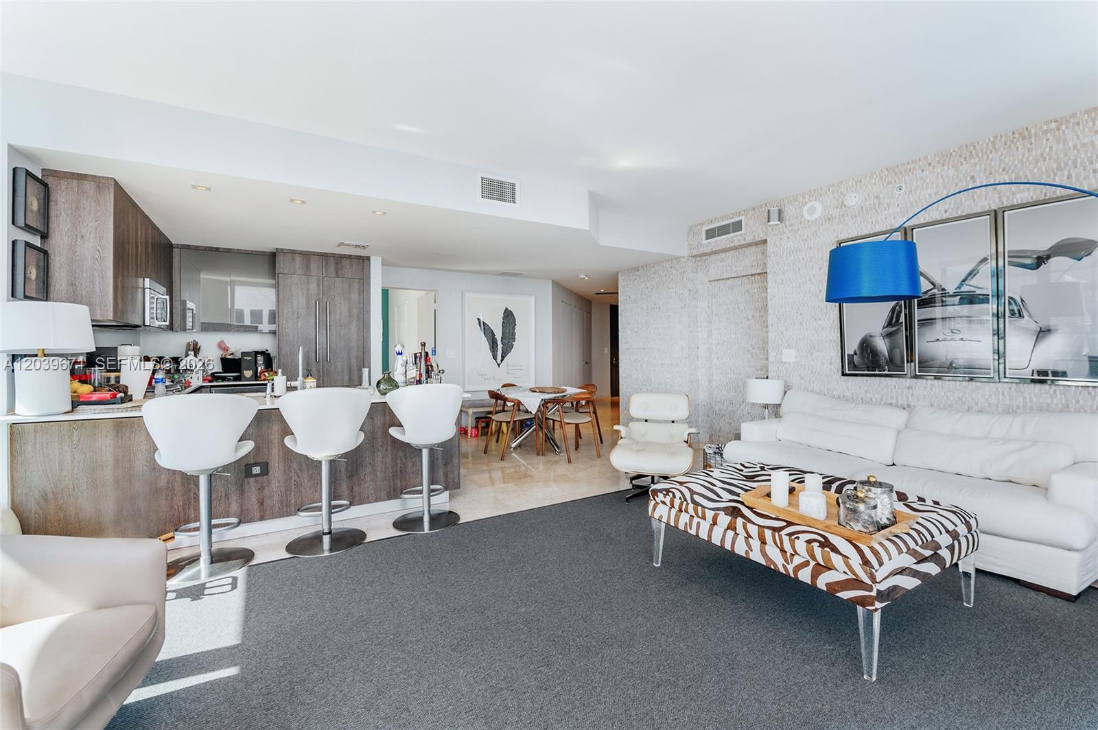 An open-concept living and dining area features a kitchen island with three white bar stools — 68 SE 6th St # 2601, Miami FL 33131, MIAMI, FL