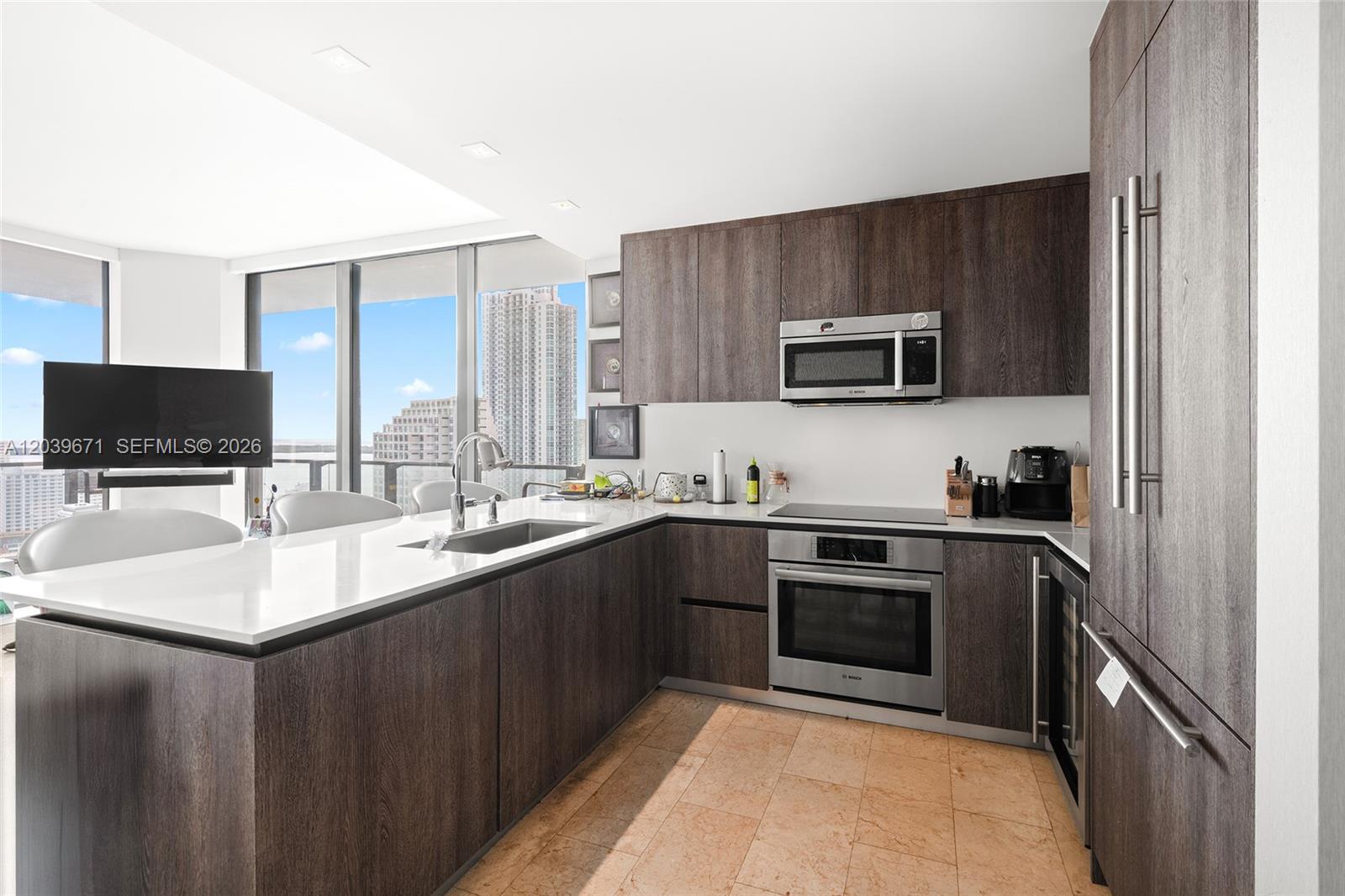 A modern kitchen features dark wood cabinetry, stainless steel appliances, and a white countertop island — 68 SE 6th St # 2601, Miami FL 33131, MIAMI, FL