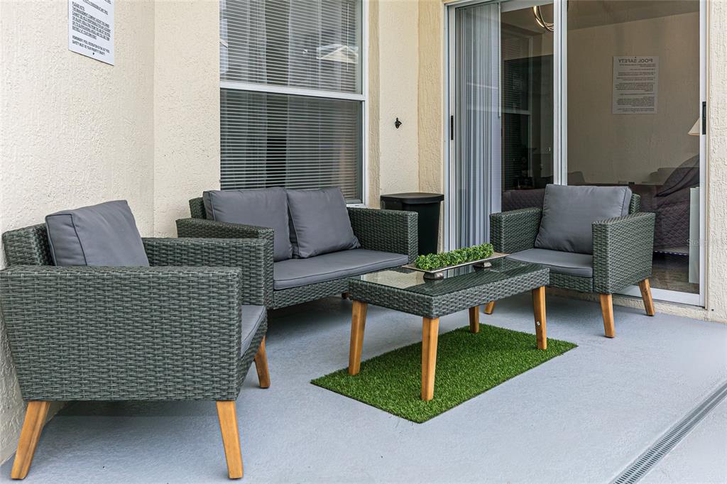A patio features gray wicker furniture, a glass-topped coffee table, and a small artificial grass rug — 146 BAYSWATER LANE, DAVENPORT, FL