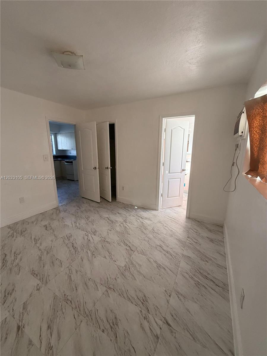 A room with white walls, marble-patterned tile flooring, two doorways, and a window air conditioner — 154 W 26th St # 2, Hialeah FL 33010, HIALEAH, FL