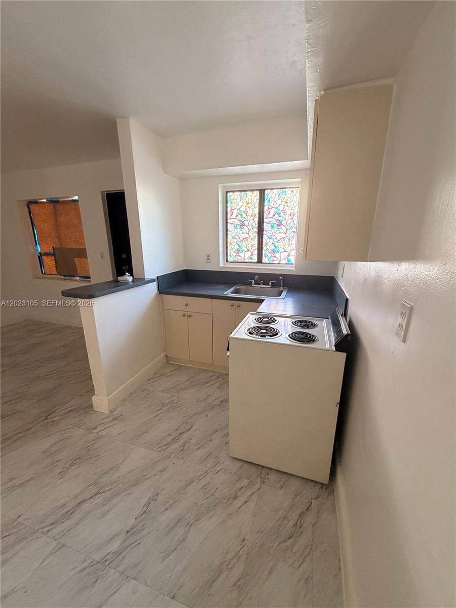 A small kitchen features light-colored cabinets, a dark countertop, a white stove, and tiled flooring — 154 W 26th St # 2, Hialeah FL 33010, HIALEAH, FL