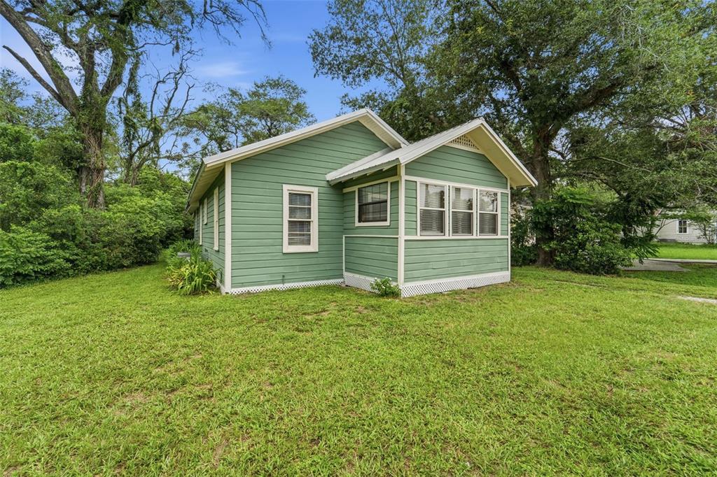 A green, single-story house with white trim and a metal roof sits on a lawn — 316 S AMELIA AVENUE, DELAND, FL