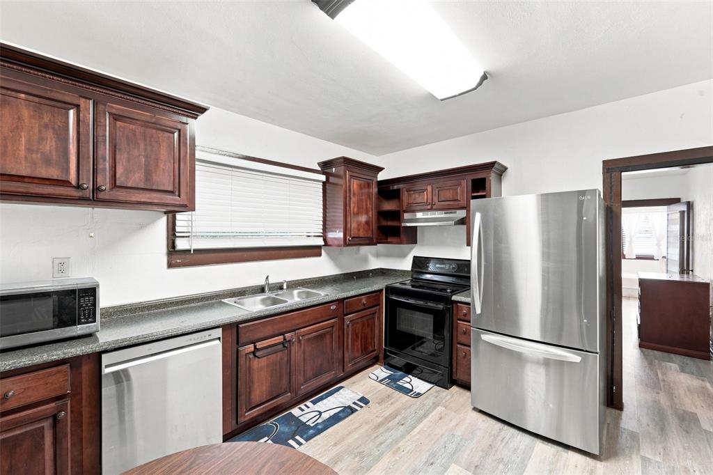 A kitchen features dark wood cabinets, stainless steel appliances, and light-colored wood-look flooring — 316 S AMELIA AVENUE, DELAND, FL