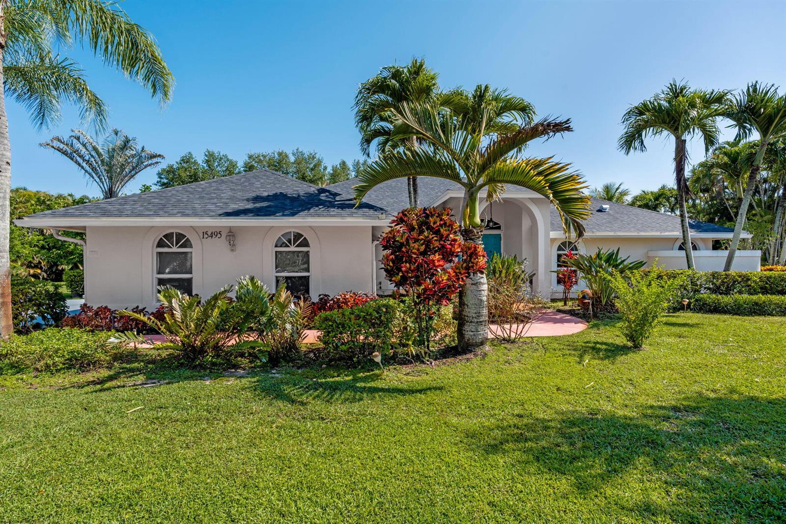 A single-story house with a gray roof, white stucco walls, and tropical landscaping — 15495 Rolling Meadows Circle, Wellington FL 33414, WELLINGTON, FL