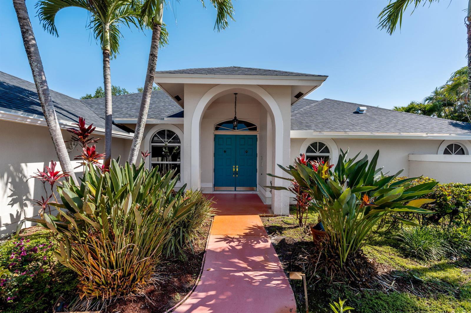 The exterior of a house features a teal double door entrance under an arched portico — 15495 Rolling Meadows Circle, Wellington FL 33414, WELLINGTON, FL