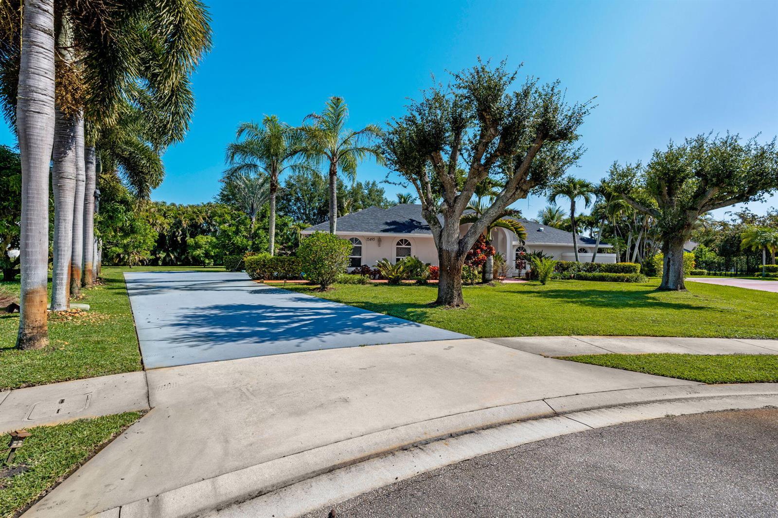 A single-story house with a blue driveway, palm trees, and a large lawn — 15495 Rolling Meadows Circle, Wellington FL 33414, WELLINGTON, FL
