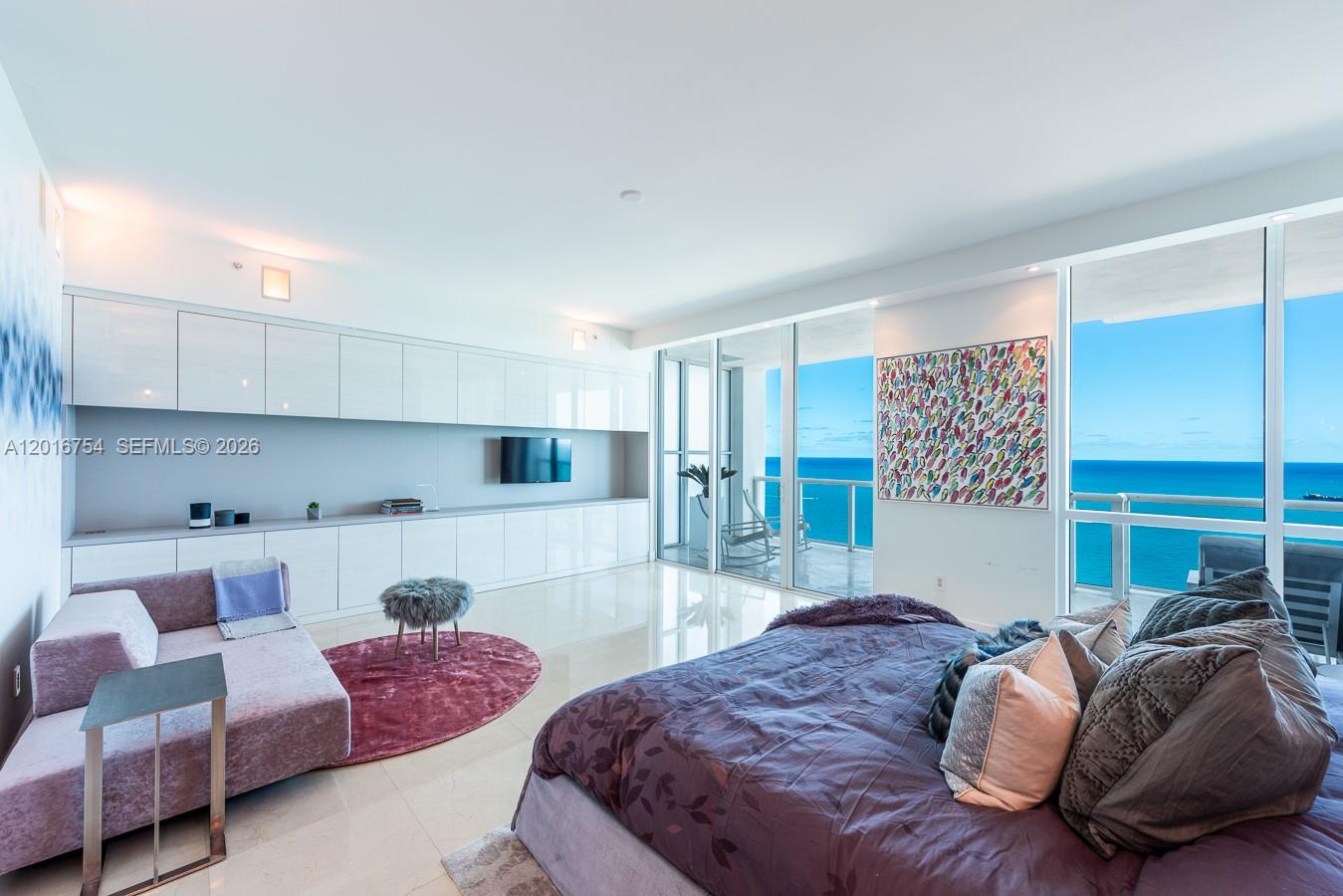 A modern bedroom features a purple bed, a seating area, and floor-to-ceiling ocean views — 50 S Pointe Dr # 3302, Miami Beach FL 33139, MIAMI BEACH, FL