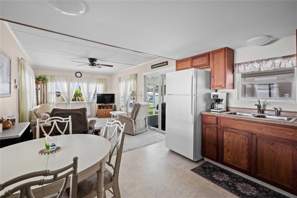 An open-concept kitchen and living area featuring wood cabinets, a white refrigerator, and dining table — 37250 BEVERLY AVENUE, ZEPHYRHILLS, FL