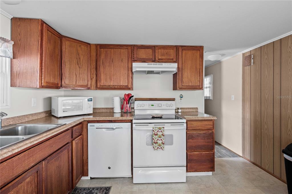 A kitchen features wood cabinets, white appliances, a laminate countertop, and wood-paneled walls — 37250 BEVERLY AVENUE, ZEPHYRHILLS, FL