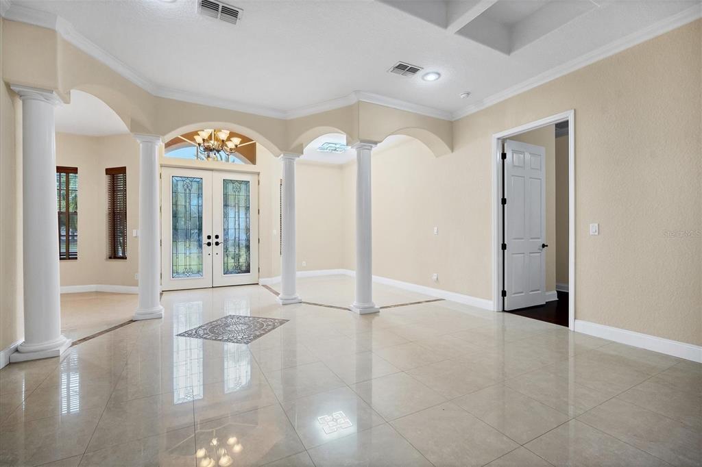 A bright foyer features white columns, arched entryways, tile flooring, and double glass front doors — 2780 BETHEL COURT S, ST PETERSBURG, FL