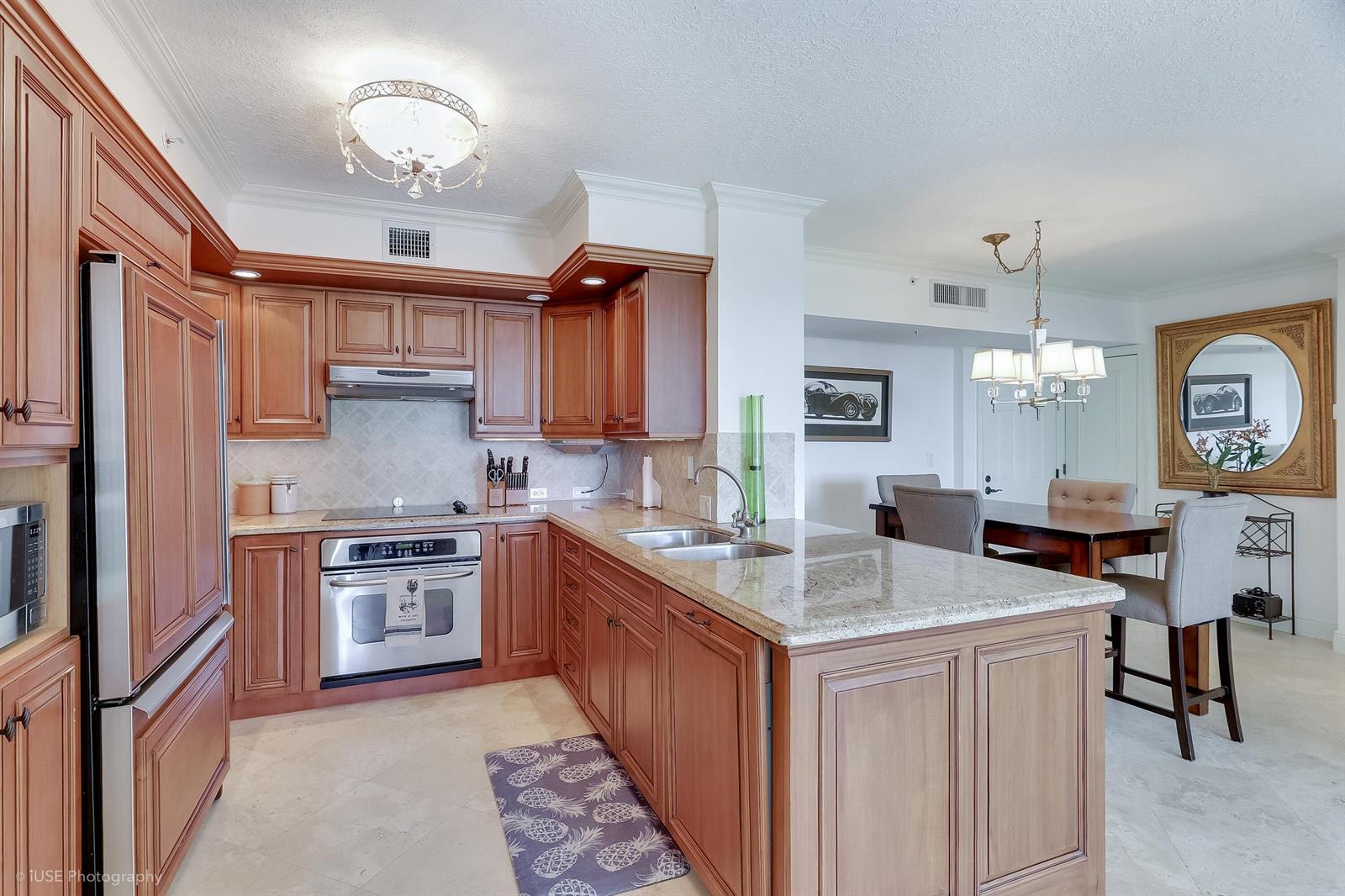 A kitchen with wood cabinets, granite countertops, and stainless steel appliances opens to a dining area — 651 Okeechobee Boulevard # 509, West Palm Beach FL 33401, WEST PALM BEACH, FL