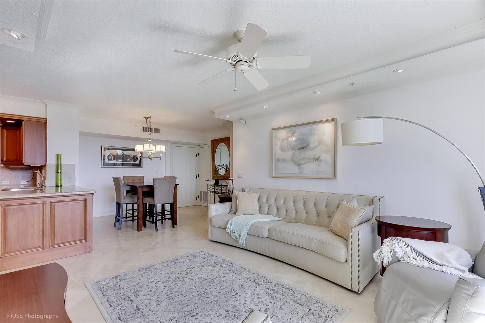 A living room with a tufted sofa, dining area, and kitchen with wooden cabinets — 651 Okeechobee Boulevard # 509, West Palm Beach FL 33401, WEST PALM BEACH, FL
