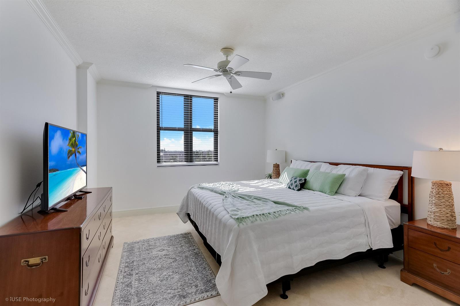A bedroom features a bed with white bedding, a wooden dresser, and a ceiling fan — 651 Okeechobee Boulevard # 509, West Palm Beach FL 33401, WEST PALM BEACH, FL