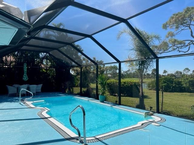 A screened-in swimming pool sits on a blue patio overlooking a grassy yard and trees — 2091 KING TARPON DRIVE, PUNTA GORDA, FL