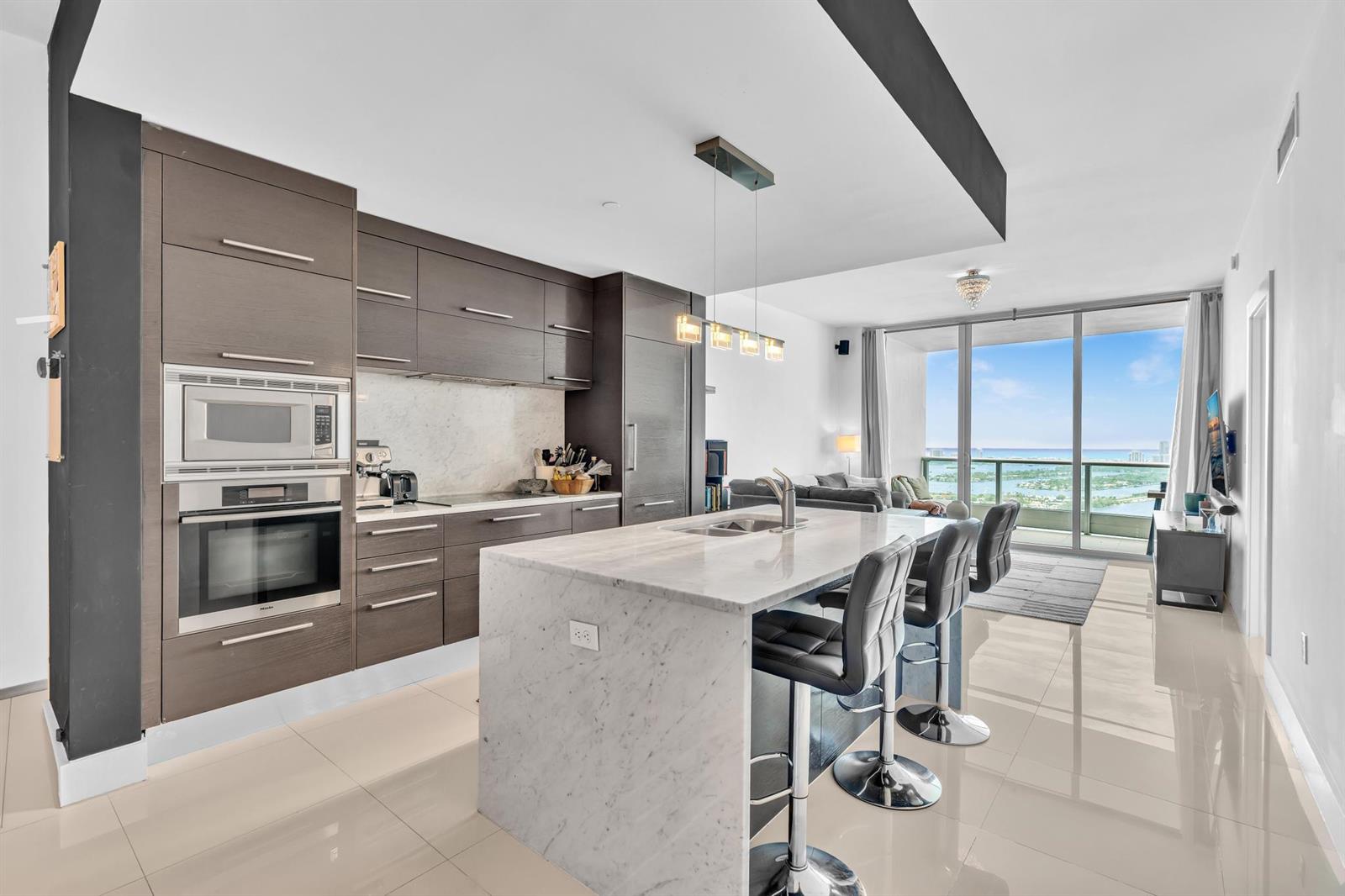 A modern kitchen features dark wood cabinetry, a marble island, and floor-to-ceiling balcony windows — 900 Biscayne Boulevard # 4703, Miami FL 33132, MIAMI, FL