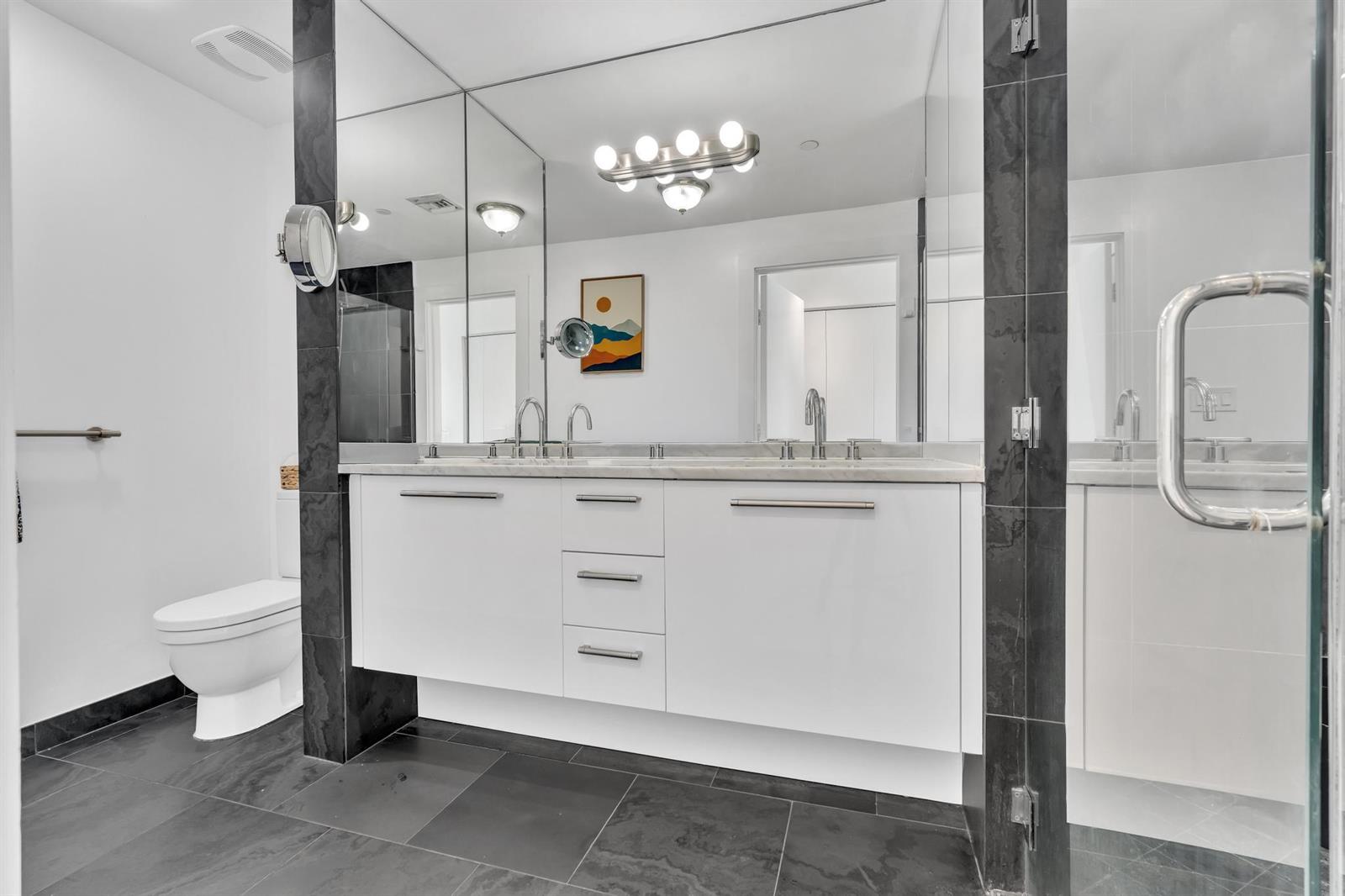A modern bathroom features a double vanity, dark tile flooring, and a large wall mirror — 900 Biscayne Boulevard # 4703, Miami FL 33132, MIAMI, FL