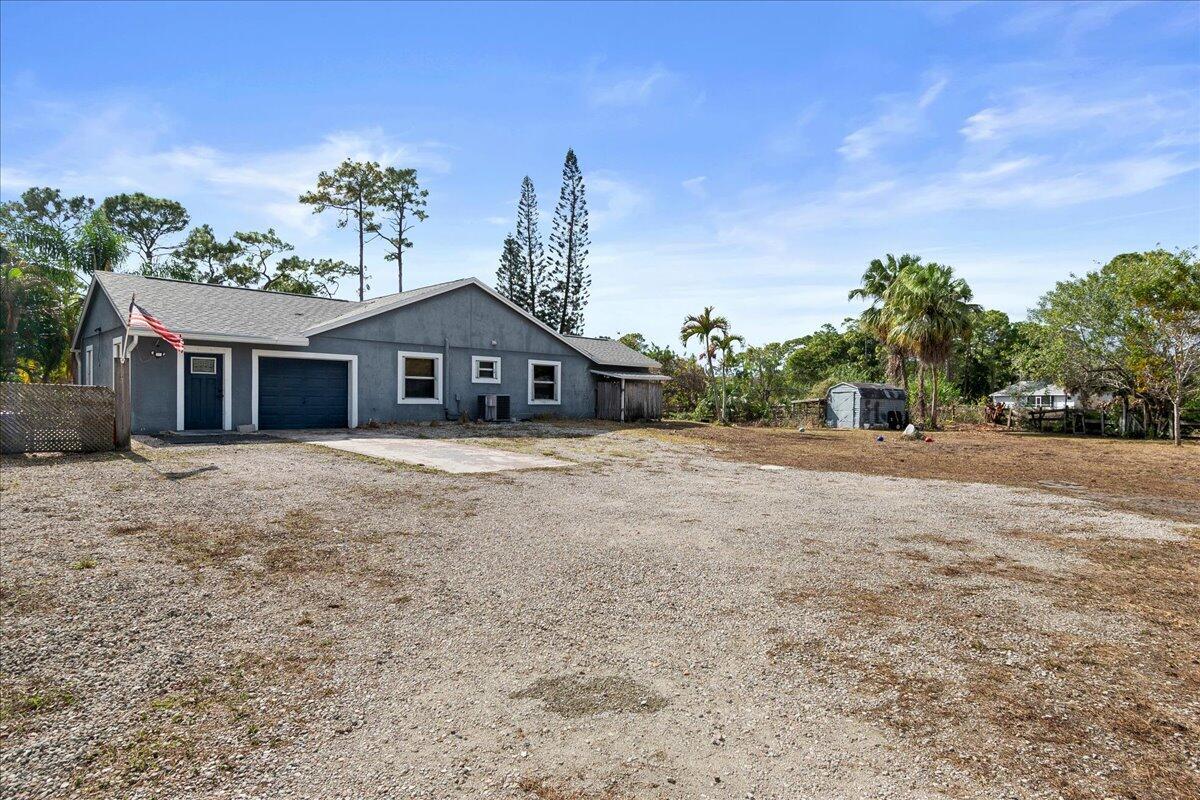 A gray single-story house with a gravel driveway and an American flag — 14537 77th Place N, Loxahatchee FL 33470, LOXAHATCHEE, FL
