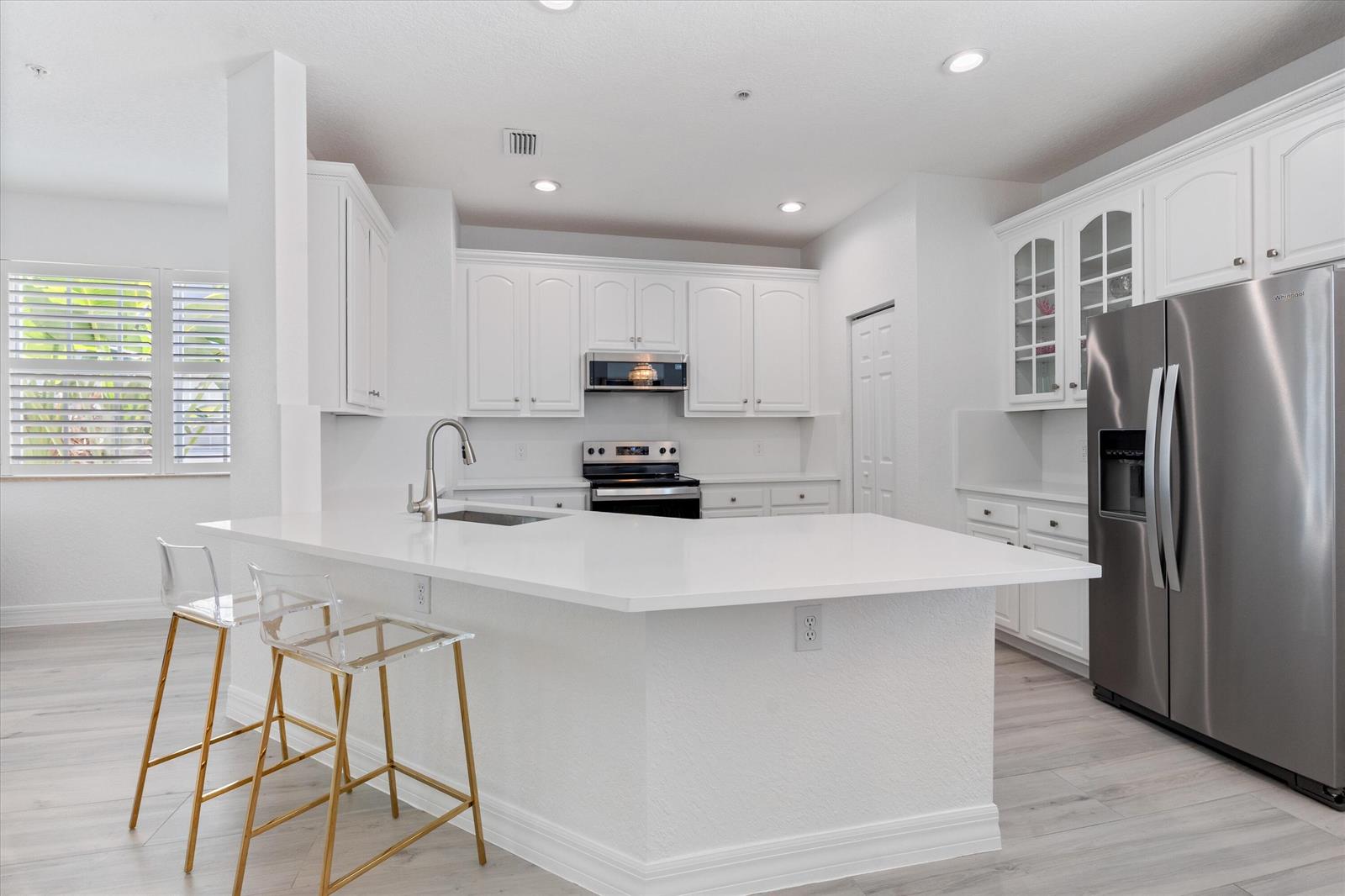 A white kitchen features a large island, stainless steel appliances, and light wood-look flooring — 295 NE 5th Avenue # 32, Delray Beach FL 33483, DELRAY BEACH, FL