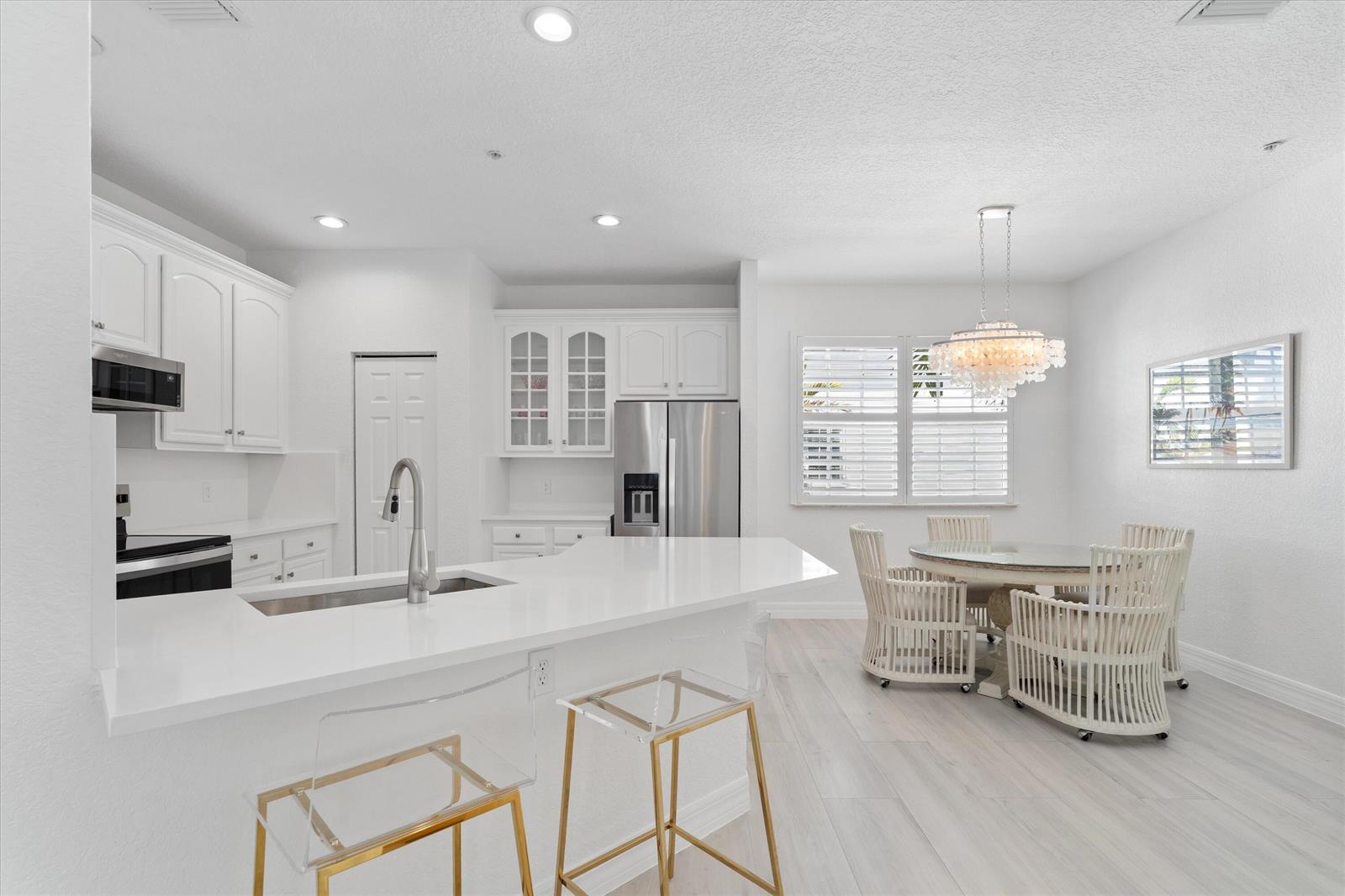 A bright kitchen and dining area features white cabinetry, quartz countertops, and a glass chandelier — 295 NE 5th Avenue # 32, Delray Beach FL 33483, DELRAY BEACH, FL