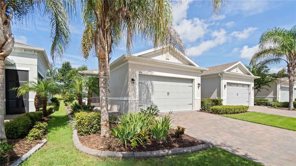 A view of suburban houses with paved driveways, manicured landscaping, and palm trees under blue skies — 1896 FLORA PASS PLACE, KISSIMMEE, FL