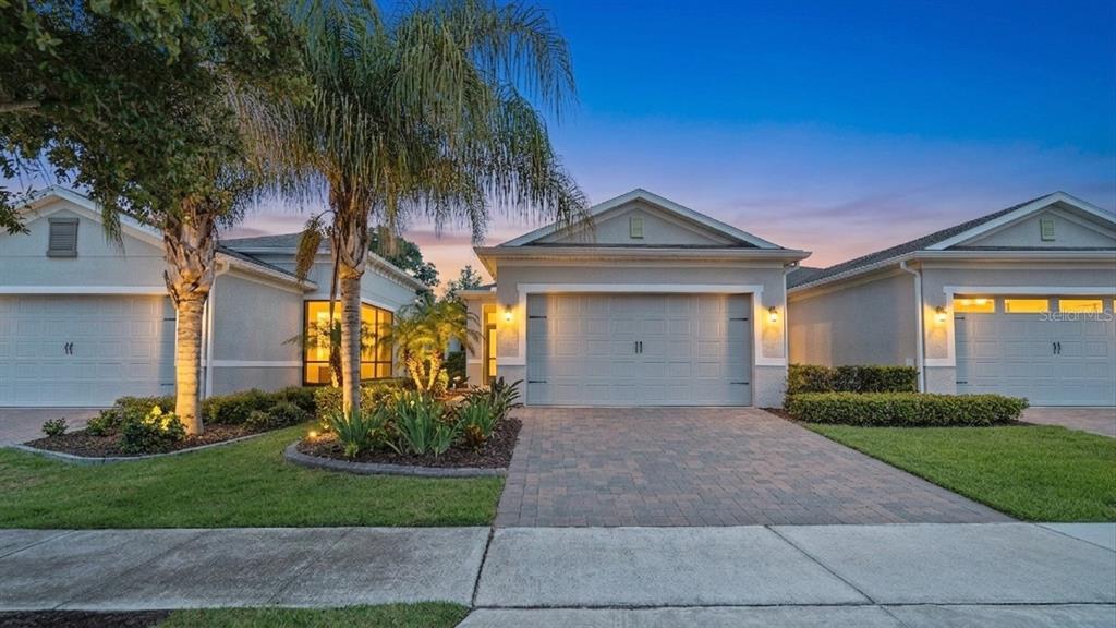 A row of three single-story houses with gray garages and paved driveways at dusk — 1896 FLORA PASS PLACE, KISSIMMEE, FL