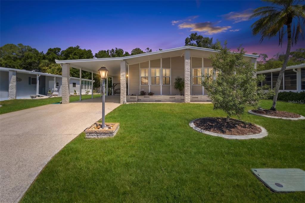 A single-story manufactured home features a tan exterior, a covered carport, and a front lawn — 209 VISTORIA DRIVE, NORTH PORT, FL