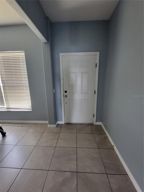 A room with light blue walls, tile flooring, a window with blinds, and a white door — 2734 ROCHELLE DRIVE, WINTER HAVEN, FL