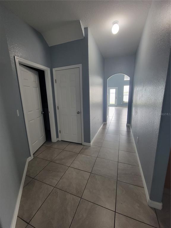 A hallway with light blue walls and tan tile flooring leads toward an arched doorway — 2734 ROCHELLE DRIVE, WINTER HAVEN, FL