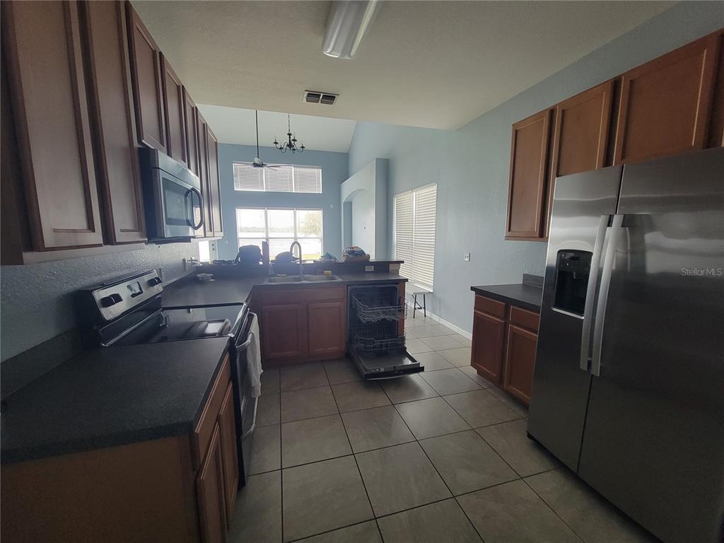 A kitchen features wood cabinets, stainless steel appliances, dark countertops, and tile flooring — 2734 ROCHELLE DRIVE, WINTER HAVEN, FL