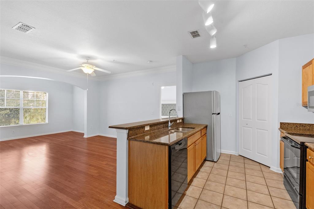 A kitchen with granite countertops and wood cabinets overlooks an adjacent living area with flooring — 4207 S DALE MABRY HIGHWAY UNIT 5310, TAMPA, FL