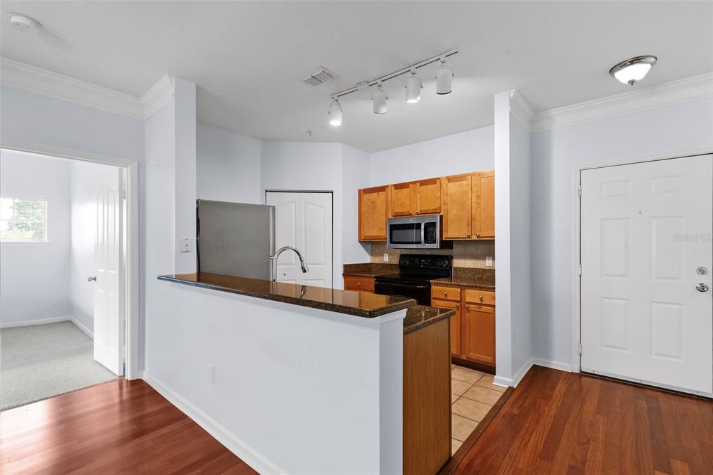 A kitchen with wood cabinets, granite countertops, and stainless steel appliances opens to a living area — 4207 S DALE MABRY HIGHWAY UNIT 5310, TAMPA, FL