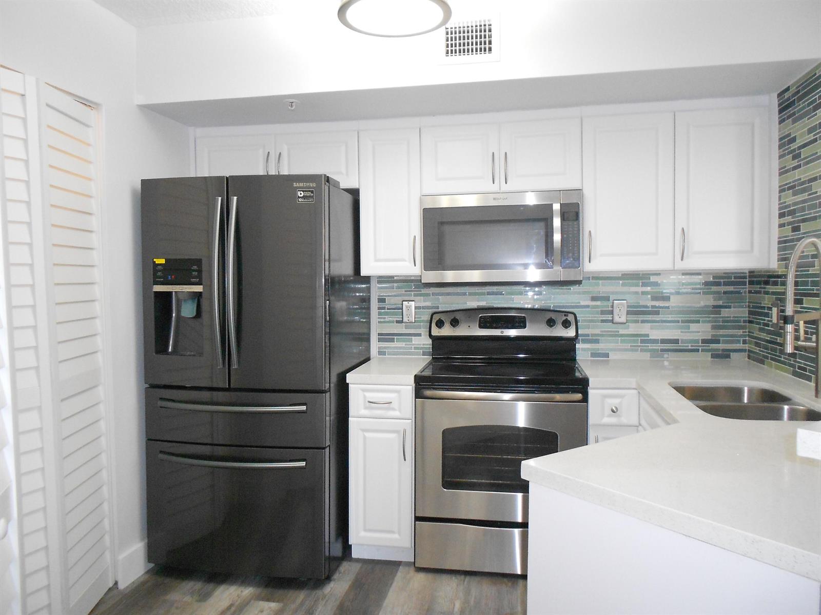 A kitchen featuring white cabinets, stainless steel appliances, a dark refrigerator, and a blue-tiled backsplash — 1000 Scotia Drive # 304, Hypoluxo FL 33462, HYPOLUXO, FL