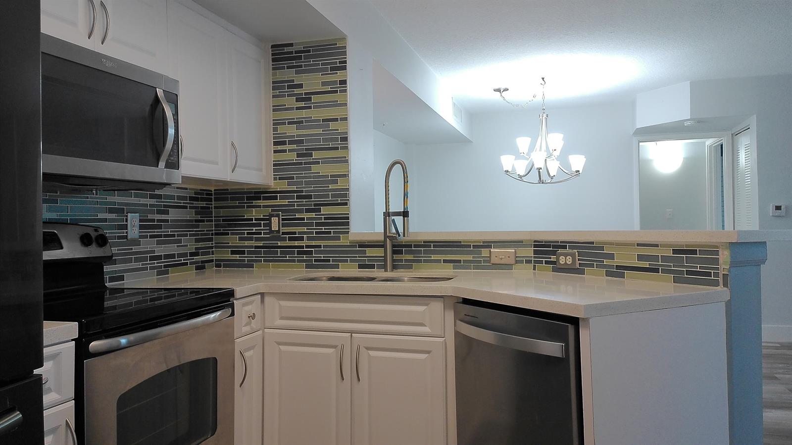 A kitchen features white cabinets, stainless steel appliances, and a multi-colored glass tile backsplash — 1000 Scotia Drive # 304, Hypoluxo FL 33462, HYPOLUXO, FL