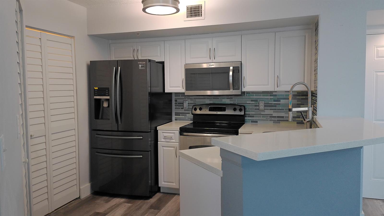 A kitchen features white cabinets, stainless steel appliances, a dark refrigerator, and a tiled backsplash — 1000 Scotia Drive # 304, Hypoluxo FL 33462, HYPOLUXO, FL