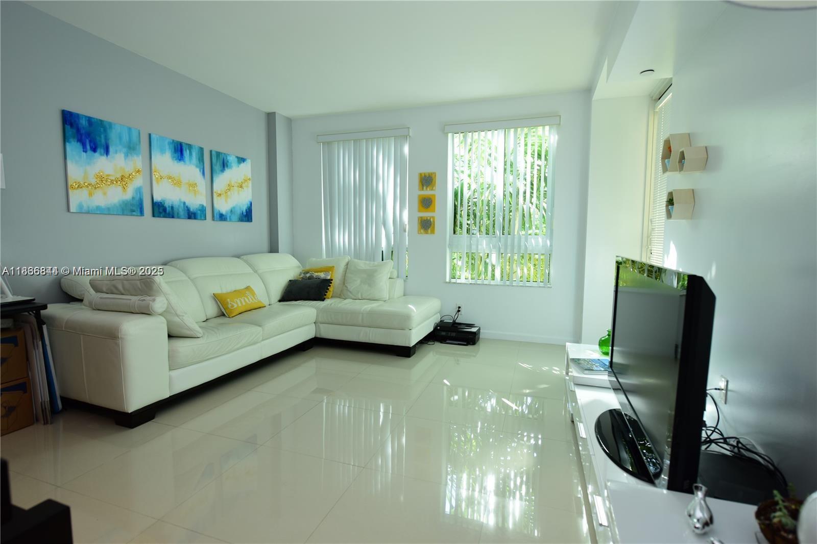 A living room features a white sectional sofa, tiled floors, and a television on a stand — 7355 SW 89th St # 622N, Miami FL 33156, MIAMI, FL